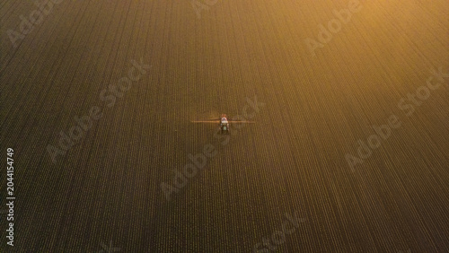 Fotografie Aerial view of crop sprayer working on a corn field at sunset