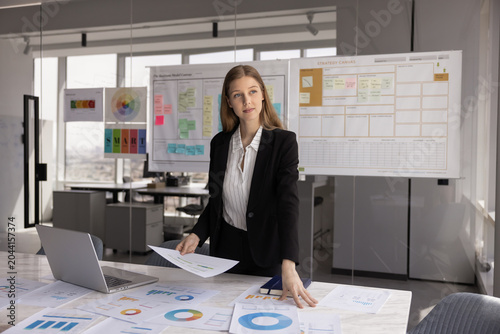 Foto Young businesswoman, project manager or coordinator working in office with data, analyzing colorful pie charts and bar graphs laid out on conference desk, prepare reports, planning strategy
