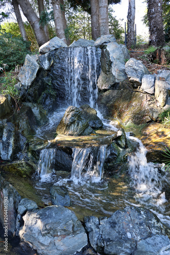 A small, multi-tiered rock waterfall cascading into a garden pond at the Rockhampton Botanic Gardens in Queensland, Australia