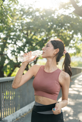 Bild auf Leinwand Happy slim asian woman drinking water after workout exercising on running track in the public park