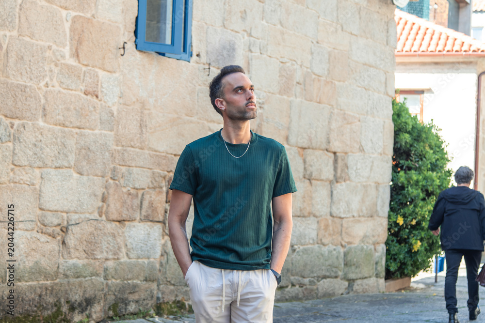 Fototapeta premium Handsome man casually walking through the city looking to the side, glancing at the houses