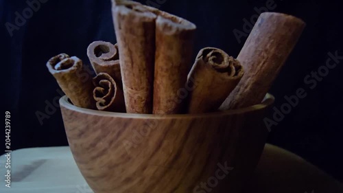 Close-up of aromatic cinnamon sticks (Cinnamomum verum) in a wooden bowl. Warm lighting highlights rich textures against a dark background. Perfect for culinary, wellness, and organic food projects.