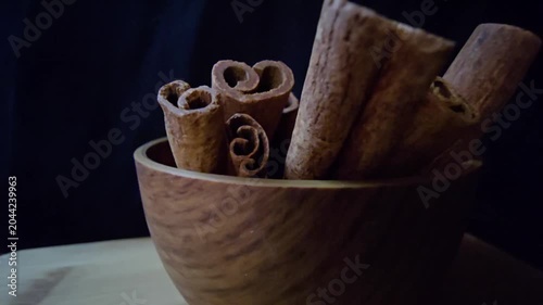 Close-up of aromatic cinnamon sticks (Cinnamomum verum) in a wooden bowl. Warm lighting highlights rich textures against a dark background. Perfect for culinary, wellness, and organic food projects.