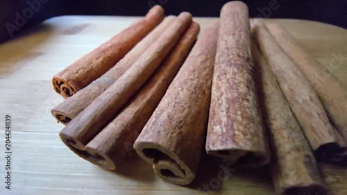 Close-up of a rustic arrangement of fragrant cinnamon sticks, scientifically known as Cinnamomum verum, resting on a natural wooden board with a blurred wooden bowl in the background. 