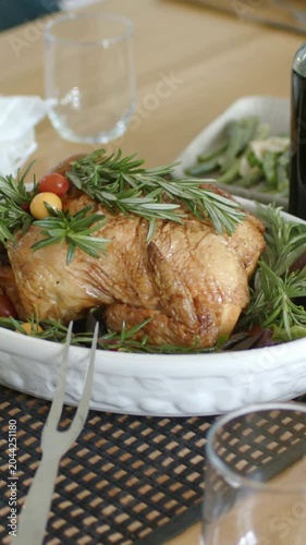 Vertical video: Pulling back cam showing roast with rosemary and fork on wood table, for serving