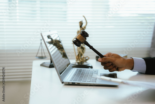 Foto A legal professional works on a laptop beside justice symbols and documents, representing legal consultation, contract review, compliance, digital law services, and business governance