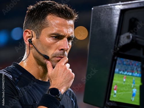 Focused soccer referee looking at var monitor during stadium football game