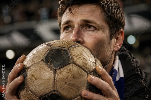 Emotional soccer fan kissing worn out old football in stadium stand