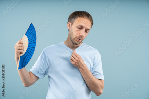 Foto Exhausted middle aged man holding hand fan while clutching shirt, breathing heavily