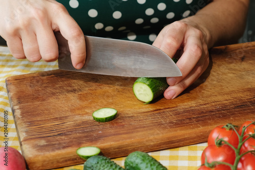 Cooking diet summer food. Woman slicing fresh cucumber to make vegetable salad