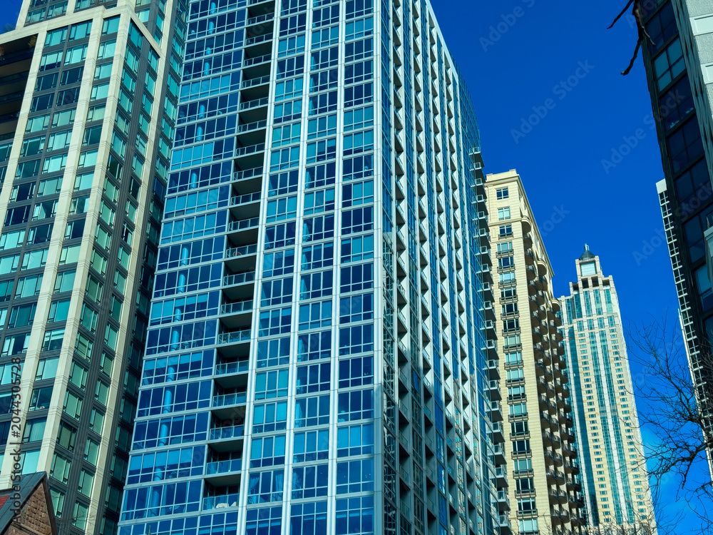 Obraz premium Modern buildings reach up to the blue sky in a bustling city on a clear day, showcasing urban architecture and city life from a low angle perspective with no people nearby