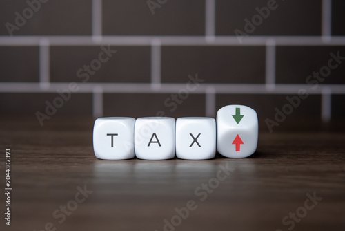 White blocks spelling the word TAX next to a tilted cube showing green down and red up arrows. Tax cuts, tax increases, financial planning, and government fiscal policy changes concept.