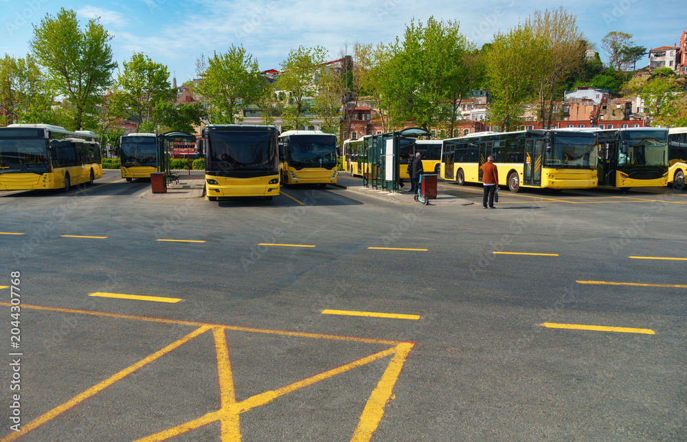 Obraz premium Public transportation buses parked at a bus station terminal in Istanbul, Turkey, with city buildings and mosque minarets visible under a clear blue sky during daytime.