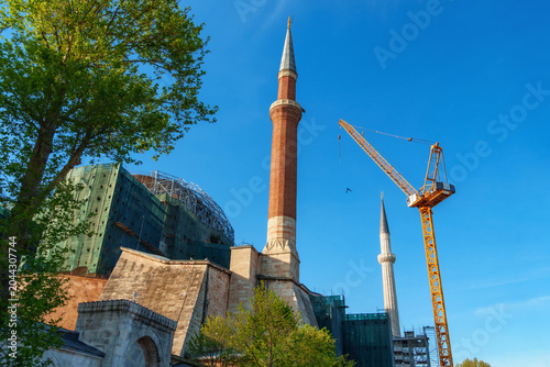 Photos Historic Hagia Sophia Mosque under restoration with construction scaffolding and a tall yellow crane against a clear blue sky in Istanbul, Turkey, landmark architecture