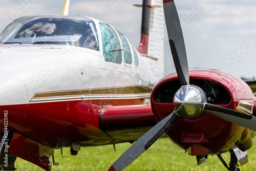 Photography Closeup of red and white twin engine aircraft polished propeller streamlined fuselage cockpit windows grassy airfield