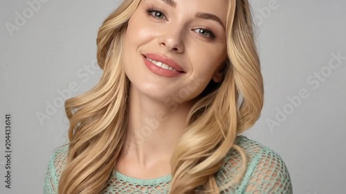 Smiling young woman with blonde hair against grey background.