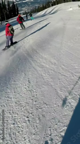 Vertical video: Chasing red snowboarder, skier filming behind as group descending on groomed run