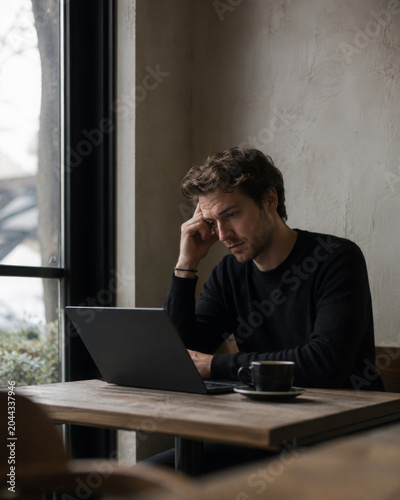 Stressed man using laptop feeling tired at cafe
