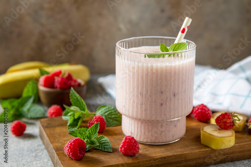 Pink raspberries and banana fruit smoothie or milk protein shake on stone tabletop. Yogurt cocktail, natural detox. Liquid ice cream. Copy space.