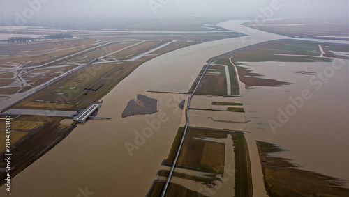 Quadro su tela Aerial view of a wide brown river flowing through a flooded landscape with field