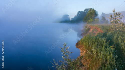 Schilderij op canvas a serene morning landscape featuring a calm river shrouded in thick, blue-tinted