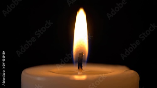 Close-up of a lit candle with a warm flame against a dark background.