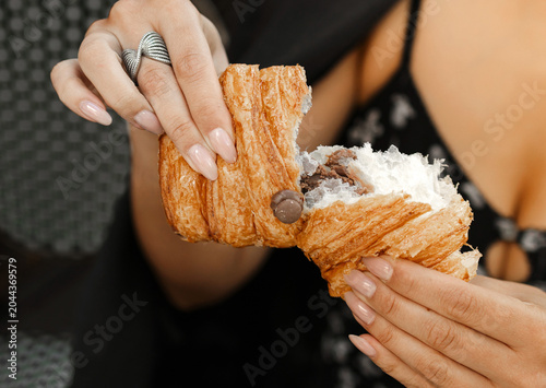 Elegant woman enjoying a chocolate croissant and coffee at an outdoor cafe terrace. Beautiful female in a grey blazer tasting French pastry. Lifestyle, breakfast or brunch concept.