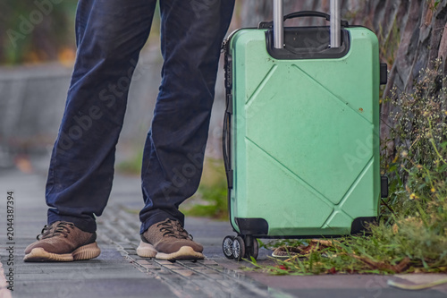 Slika na platnu Man stands beside green suitcase on sidewalk