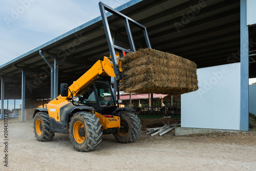 Bild auf Leinwand Telehandler lifting hay bale in agricultural farm building