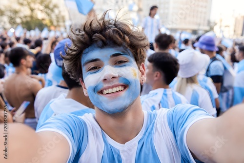 Young man with argentina flag face paint taking a selfie in a crowd of soccer fans celebrating victory