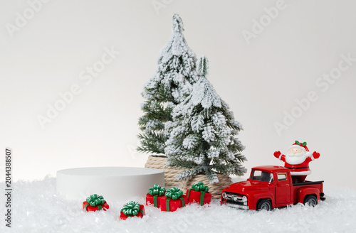 Konstfotografi Festive Christmas product display photography featuring a white cylindrical podium, snow-covered pine tree, red truck, Santa Claus figurine, and wrapped gift boxes arranged on artificial snow