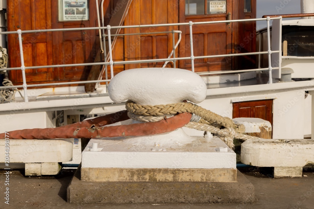 Obraz premium Thick mooring ropes and a red hose secured to a white bollard on the wharf in Auckland, New Zealand for a ship.