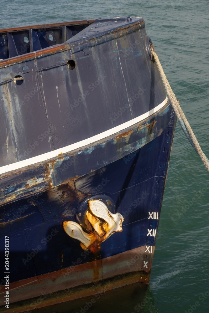 Obraz premium The bow of a dark blue ship, featuring a rusty metal anchor and draft markings, remains docked at a harbor in New Zealand.