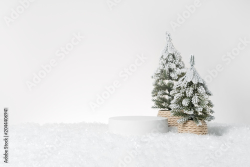 Canvastavla Winter product display scene featuring a white cylindrical podium surrounded by real snow-covered pine trees and artificial snow on a neutral studio background