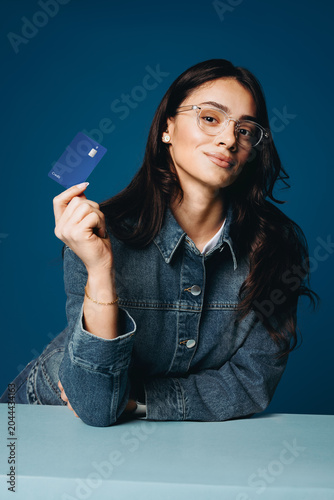 Credit card in hand, the woman poses in a blue banking studio portrait