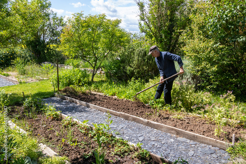 Jardinier en train d'ameublir une parcelle de terre avec un crochet dans un potager avant des plantations de légumes au printemps