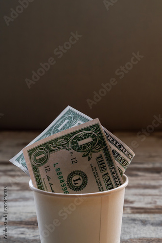 US dollar bills inside a paper cup on a wooden table, fundraising concept.