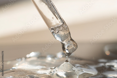 Serum in a pipette with a drop of liquid texture on a beige background with bright sunlight.