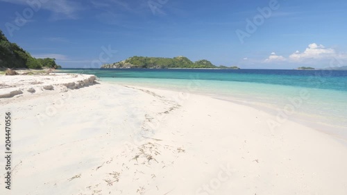 Pristine white sand beach and crystal-clear turquoise waters in Riung 17 Islands Marine Park, Flores, Indonesia, with small tropical islands on the horizon under a bright blue sky