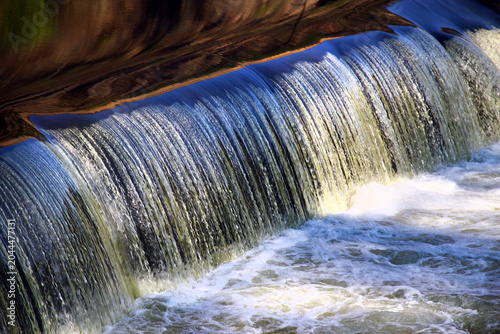 Water flowing over a small dam spillway creating a cascading waterfall and foam