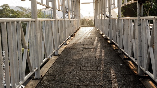 Принти на полотні Perspective of modern city transportation elements, highlighting the patterned paving stones and sturdy steel structure of the pedestrian overpass under the morning light