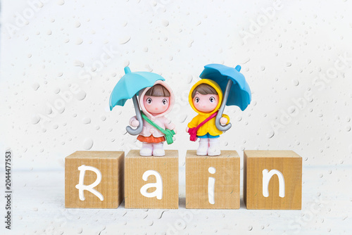 Miniature girl and boy in rain coat on wooden cube with rain drop affect, rainy season concept background