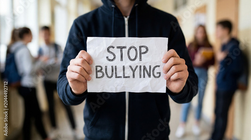Student holding stop bullying sign in school corridor, promoting anti bullying awareness and support campaign