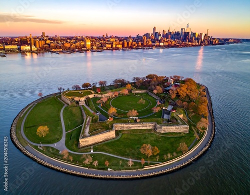Aerial view of a historic fort on a small island with a city skyline in the background at sunset