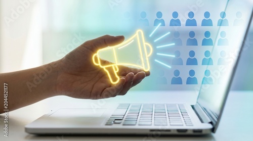 Person holding glowing digital megaphone icon floating above laptop representing digital marketing strategy and targeted online audience communication with megaphone