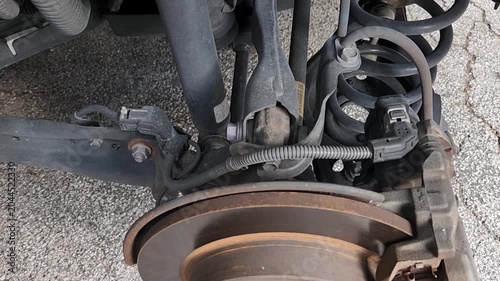 Video footage showing exposed brake rotor, brake caliper, suspension spring, shock absorber, and wheel hub after wheel removal during automotive maintenance. Detailed inspection of vehicle braking and
