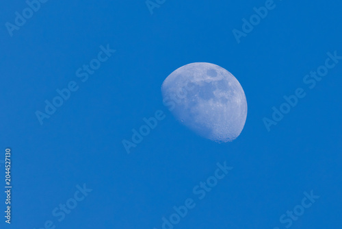 Gibbous moon visible in a clear blue daytime sky