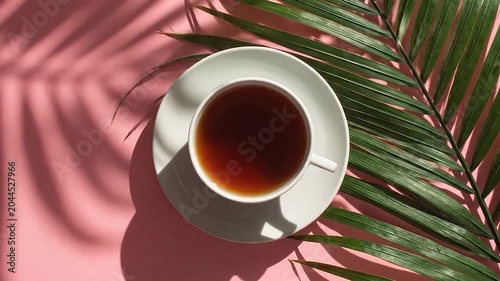 A refreshing cup of tea sits on a pink background with palm leaf shadows