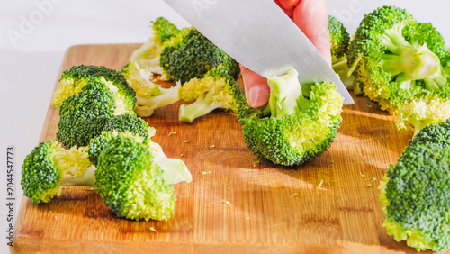 Tableau sur toile Hand slicing broccoli florets on a wooden board.