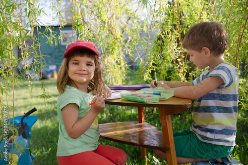 Homeschooling. Two children draw or do lessons in the garden near the house. Feral Kid Summer